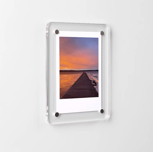 Magnetic polaroid photo frame displaying a sunset over a dock on a white background