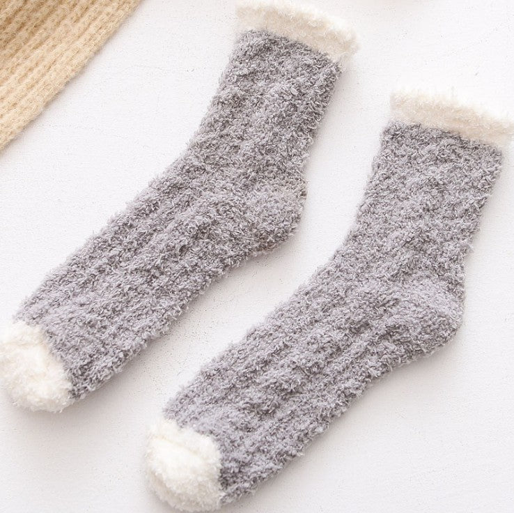 Pair of grey fuzzy socks with white toes and cuffs on a light background