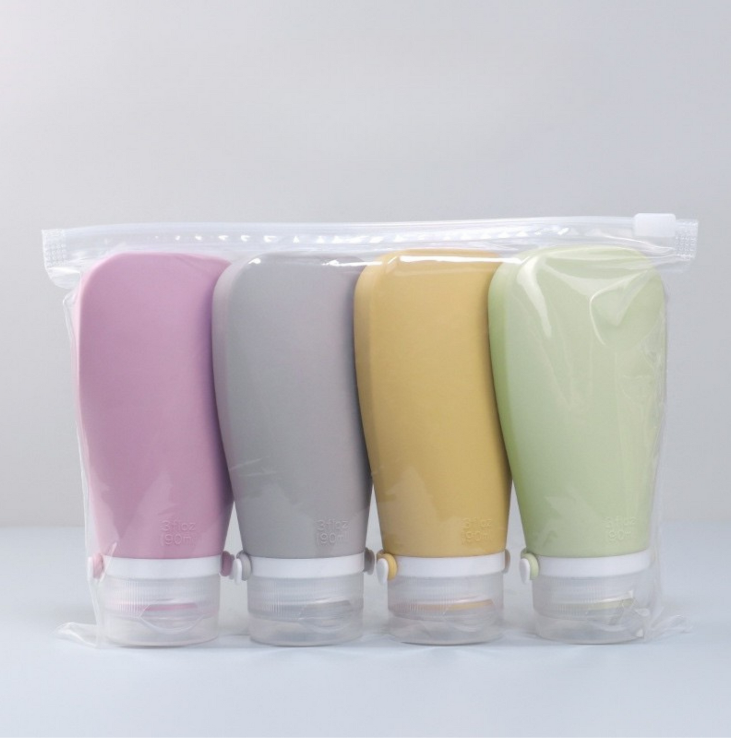 Set of four pastel-colored travel-sized bottles on a light gray background
