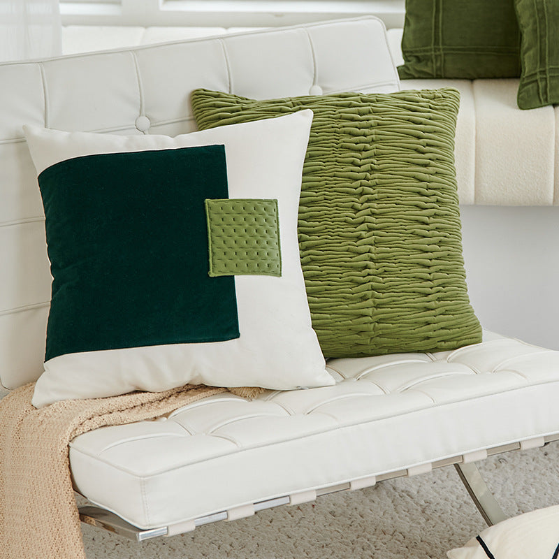 Green and white textured pillows on a white sofa with a neutral blanket.